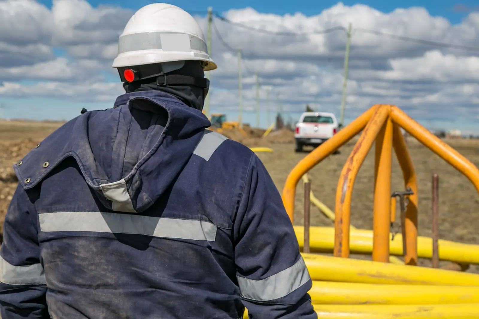 Worker in a reflective jacket and white hard hat at a pipeline site