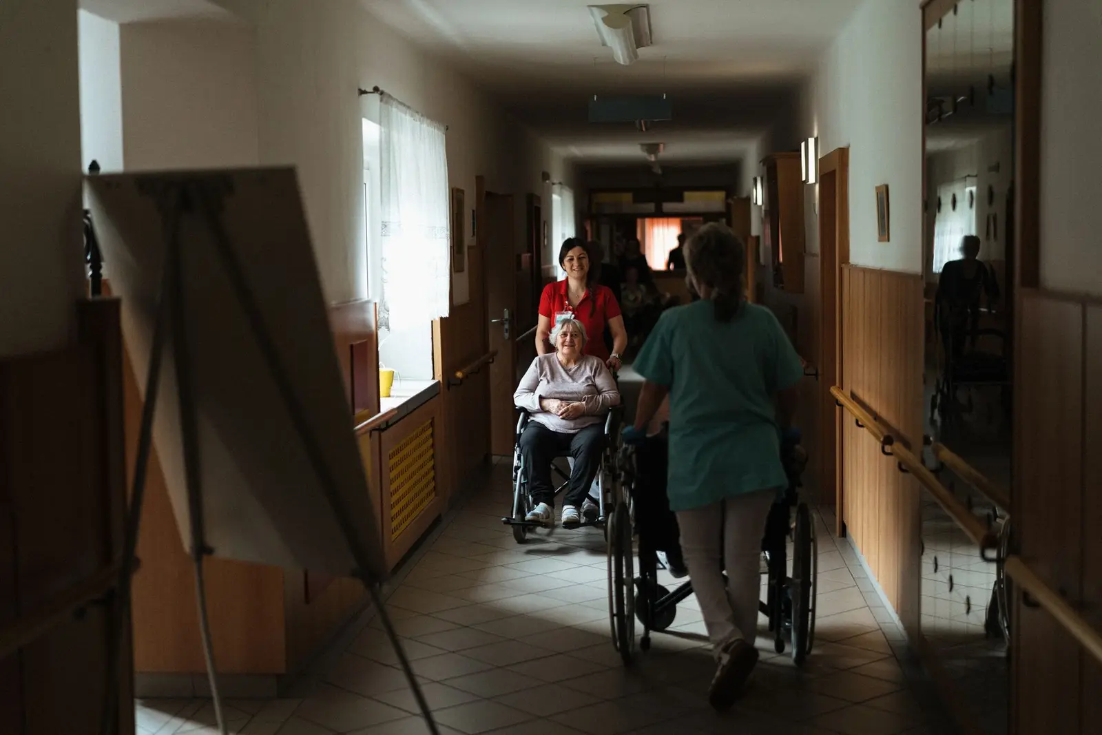 Carer in a teal tunic walking down a care-home corridor