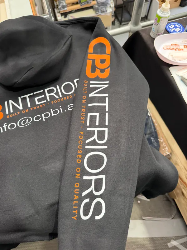 Sleeve of a dark grey hoodie printed with a vertical CPB Interiors logo