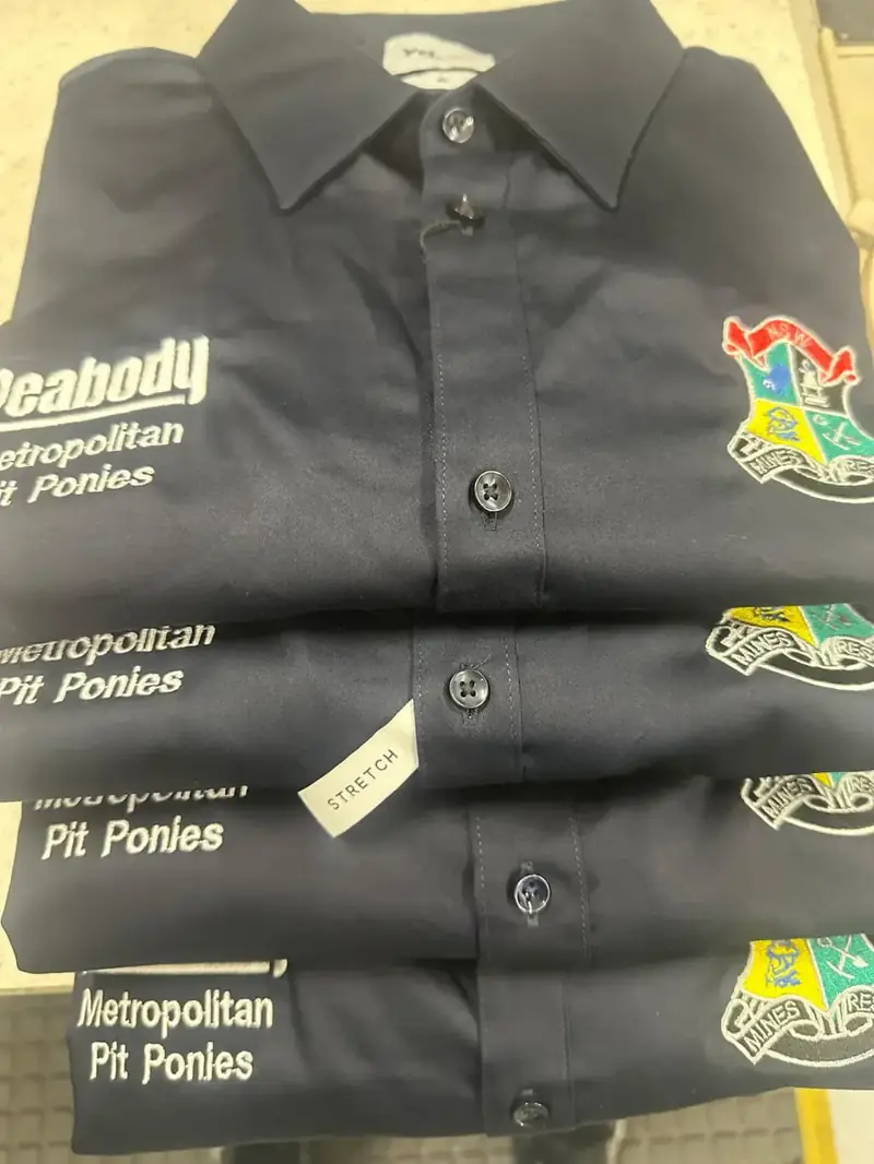 Stack of dark work shirts embroidered with team logos