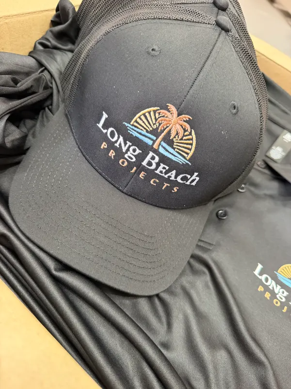 Dark cap embroidered with a Long Beach Projects palm tree logo, beside a matching polo