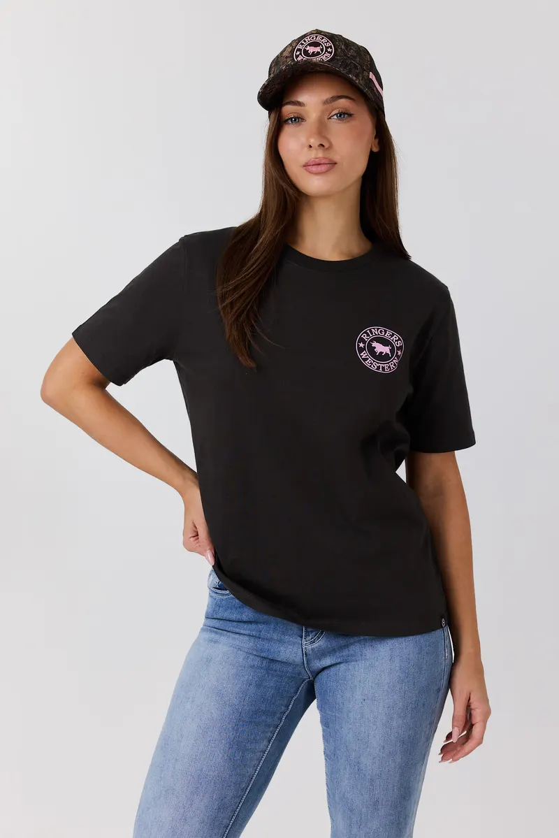 Woman in a black tee with a small pink Ringers Western crest on the chest and a camo cap